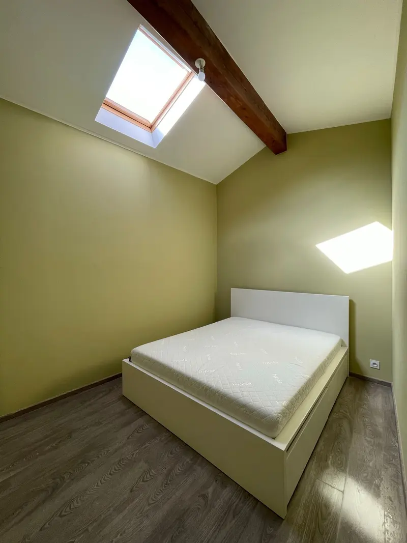 Chambre rénovée sous rampant avec fenêtre de toit et poutre apparente