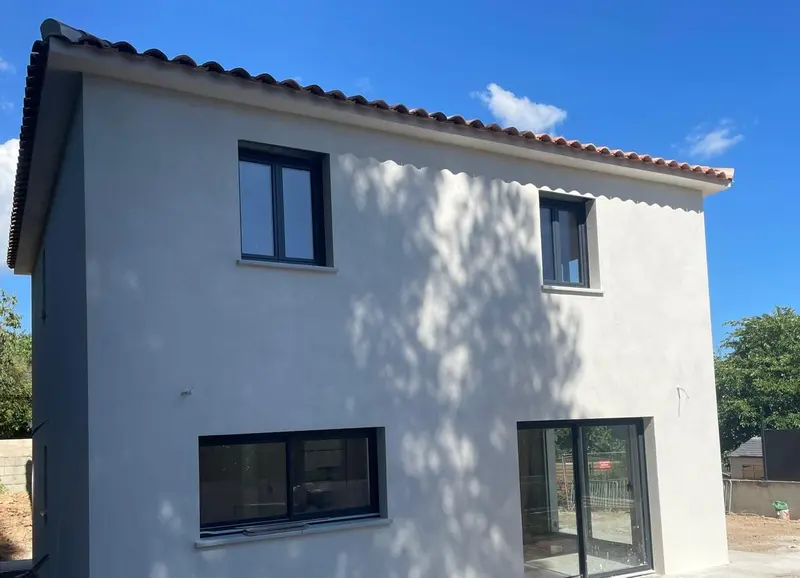 Façade arrière enduite blanche avec baie vitrée coulissante et fenêtres noires