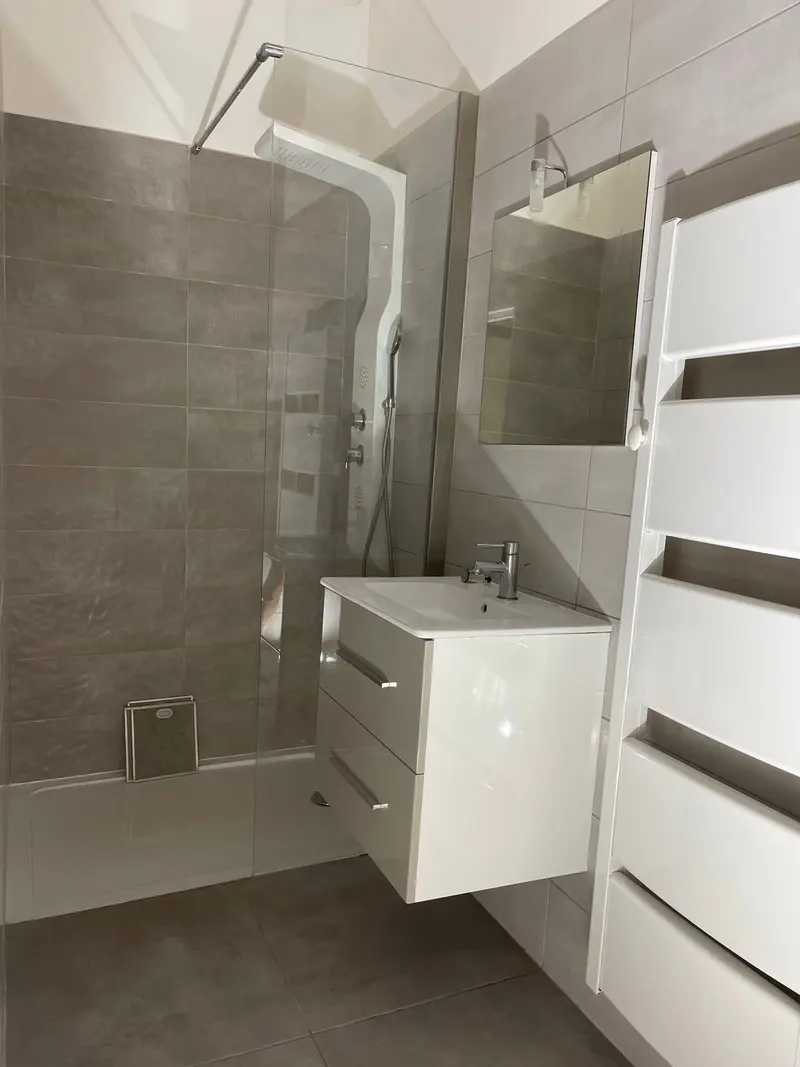 Salle d'eau avec douche vitrée, meuble vasque suspendu et carrelage gris