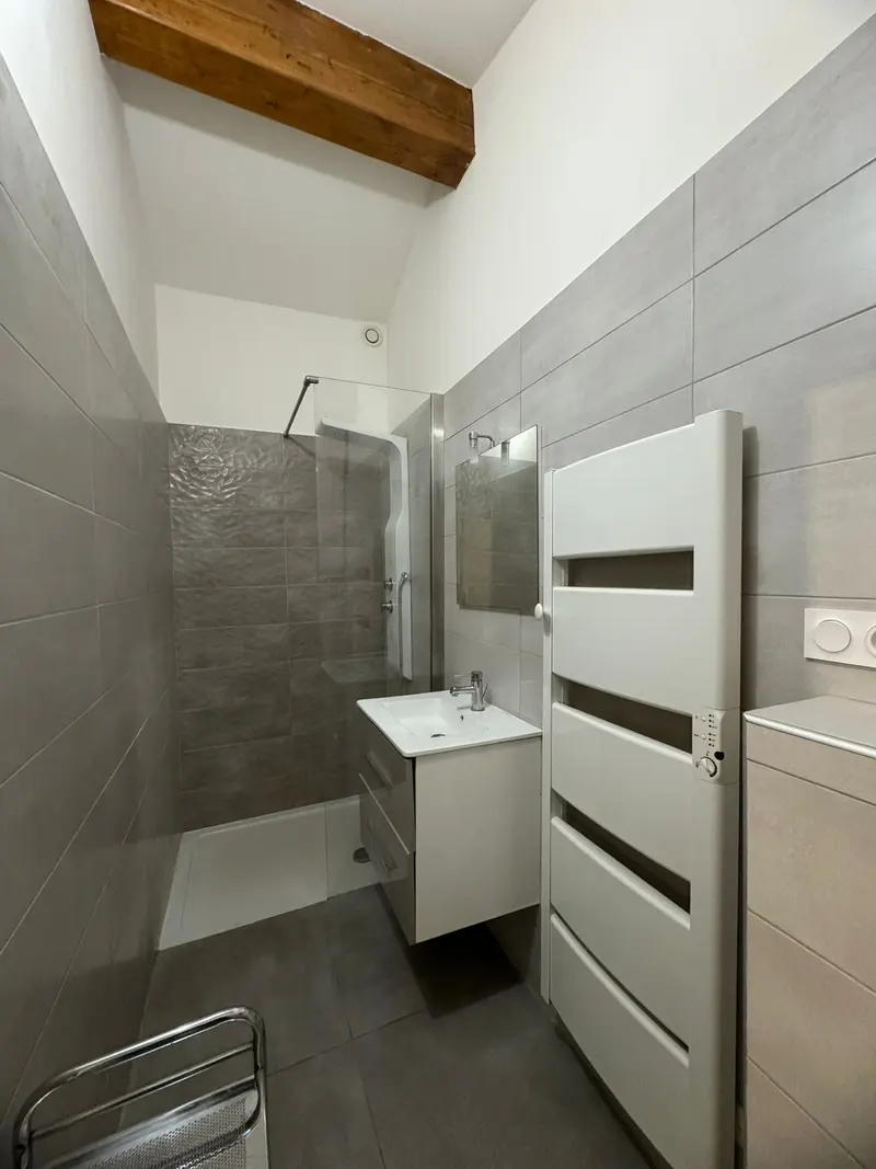 Salle d'eau rénovée avec meuble vasque blanc, douche vitrée et sèche-serviettes