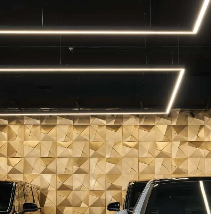 Plafond noir traversé de lignes lumineuses LED au-dessus d'un mur décoratif doré en relief